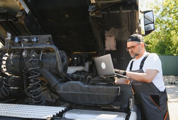 Technician using a laptop to analyse vehicle performance data, representing predictive maintenance and equipment monitoring in commercial wash operations.