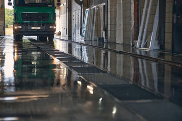 Lorry driving through a wash bay with wet flooring and drainage channels, showing the civil works required for a lorry wash system installation.