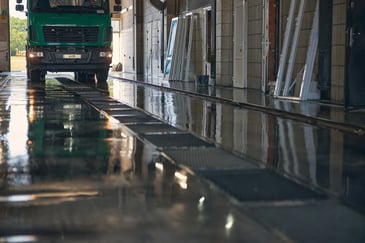Lorry driving through a wash bay with wet flooring and drainage channels, showing the civil works required for a lorry wash system installation.