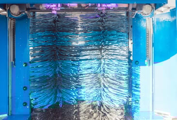 Automated vehicle wash system with rotating blue brushes in operation, representing water efficiency and reduced environmental impact.