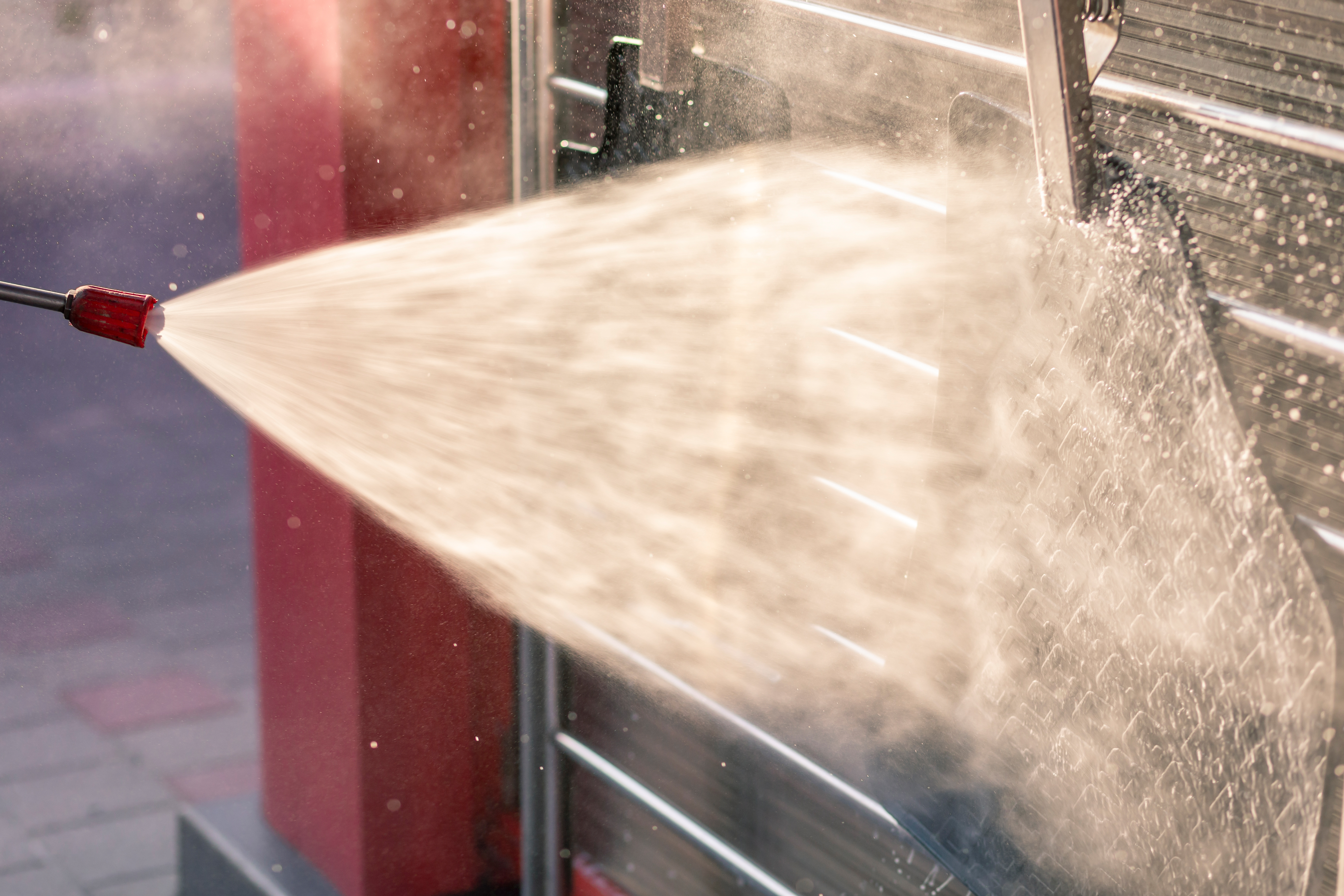 High-pressure water spray from a lance cleaning a commercial vehicle, creating overspray challenges when operating commercial vehicle wash systems in restricted areas.