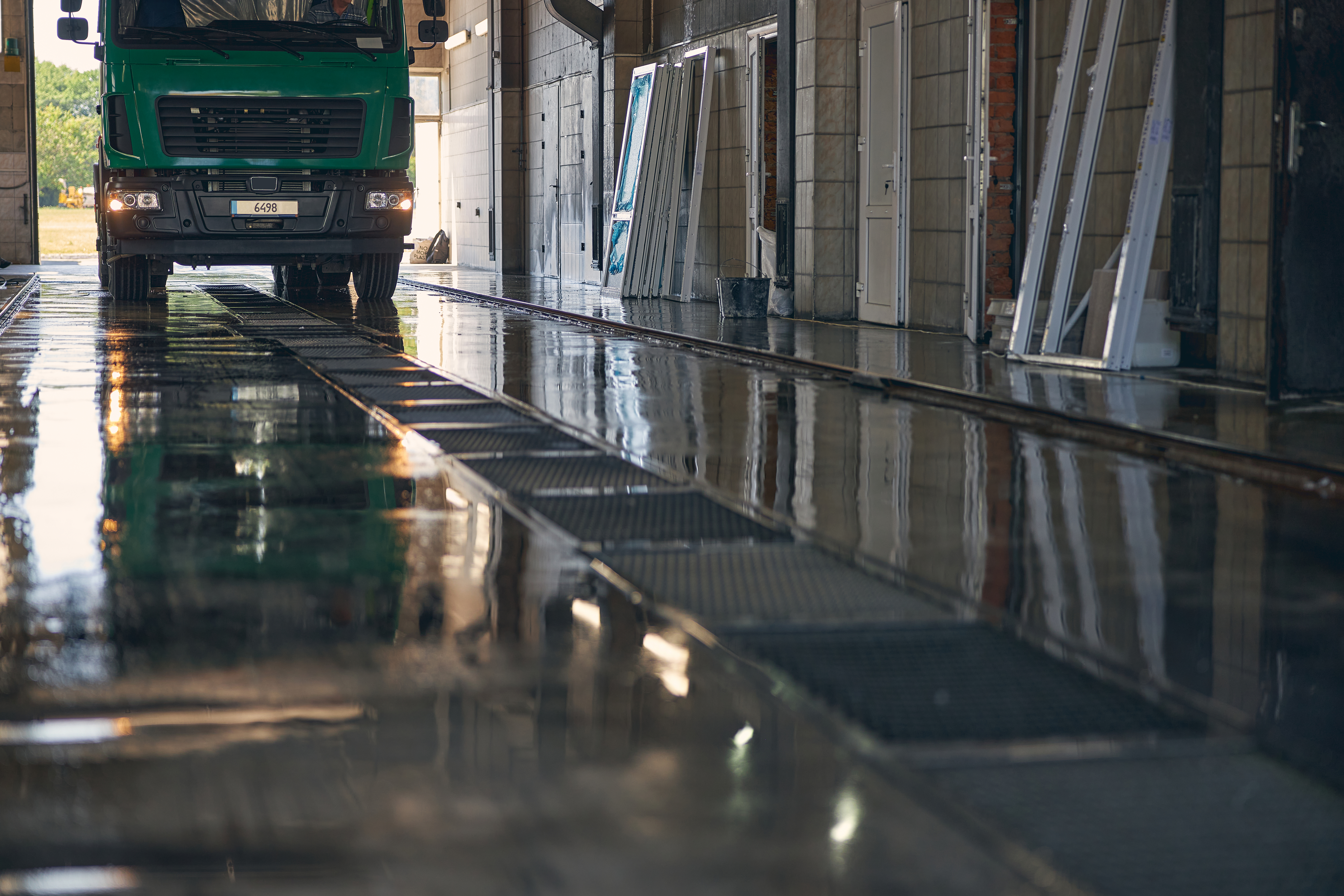  Lorry driving through a wash bay with wet flooring and drainage channels, showing the civil works required for a lorry wash system installation.