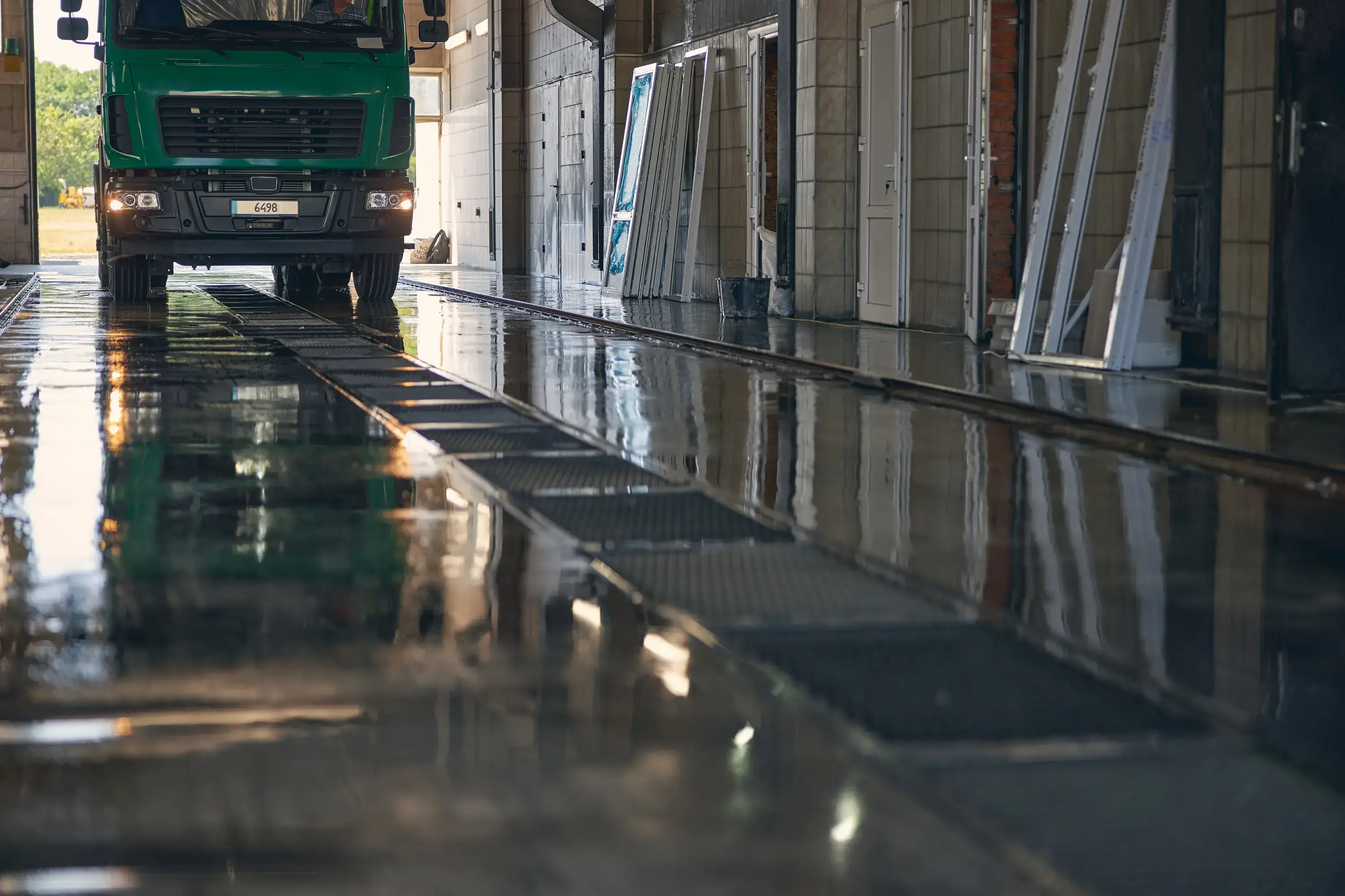 Lorry driving through a wash bay with wet flooring and drainage channels, showing the civil works required for a lorry wash system installation.